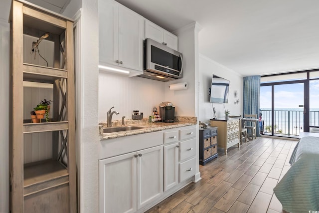 kitchen featuring wood finish floors, a sink, white cabinetry, floor to ceiling windows, and stainless steel microwave