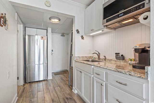 kitchen with white cabinets, wood finished floors, stainless steel appliances, a paneled ceiling, and a sink