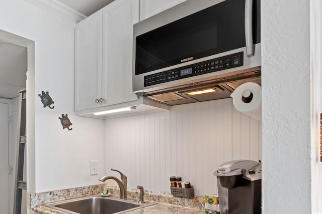 kitchen featuring white cabinets, stainless steel microwave, light countertops, and a sink