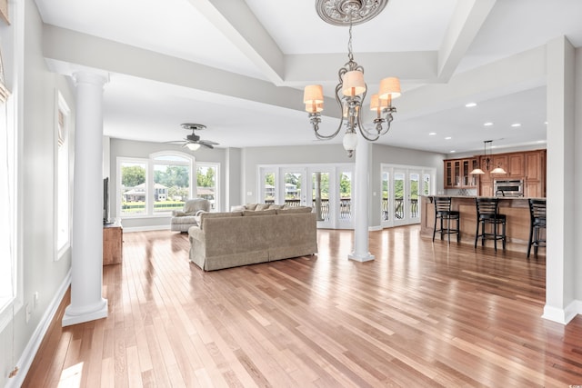 living room with ceiling fan with notable chandelier, light hardwood / wood-style floors, decorative columns, and french doors