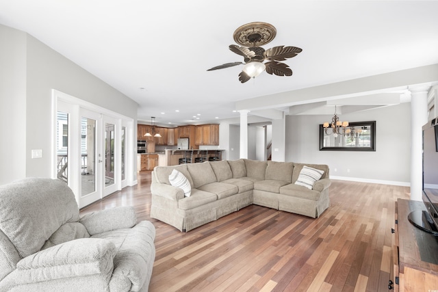 living room with ceiling fan with notable chandelier, hardwood / wood-style flooring, and decorative columns