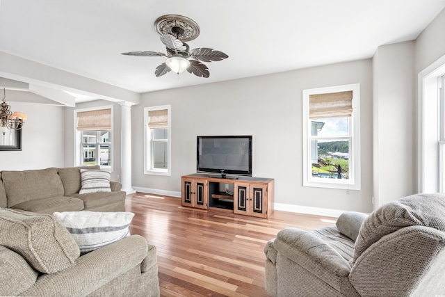 living room with ceiling fan with notable chandelier, ornate columns, and light hardwood / wood-style flooring