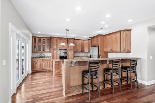 kitchen featuring light stone countertops, wood-type flooring, pendant lighting, a breakfast bar area, and appliances with stainless steel finishes