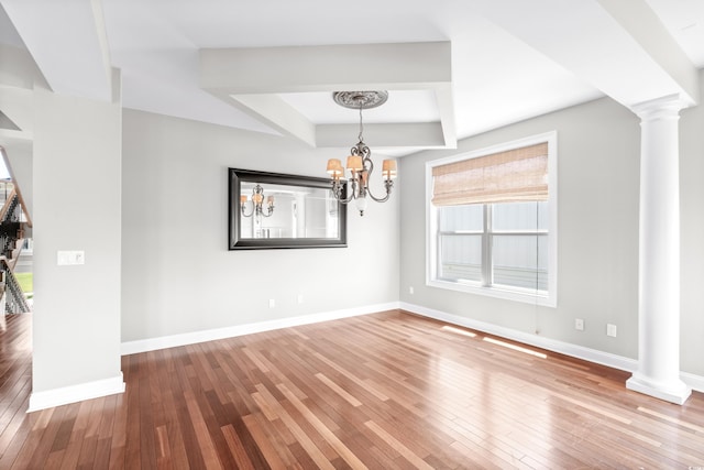 unfurnished dining area featuring a chandelier, hardwood / wood-style floors, decorative columns, and a raised ceiling