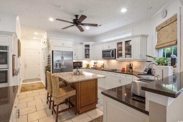 kitchen featuring a center island, dark stone countertops, black appliances, tasteful backsplash, and ceiling fan