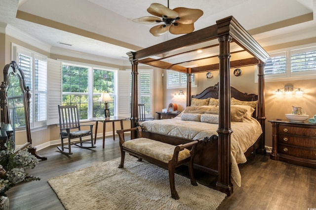 bedroom with ceiling fan, a tray ceiling, ornamental molding, and dark wood-type flooring