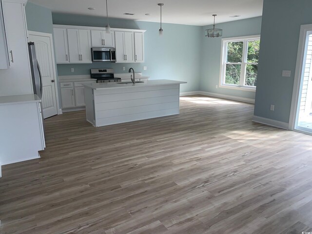 kitchen featuring light wood-type flooring, stainless steel appliances, white cabinets, hanging light fixtures, and a center island with sink