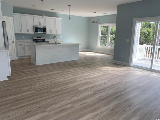 kitchen featuring stainless steel appliances, an island with sink, white cabinets, and decorative light fixtures