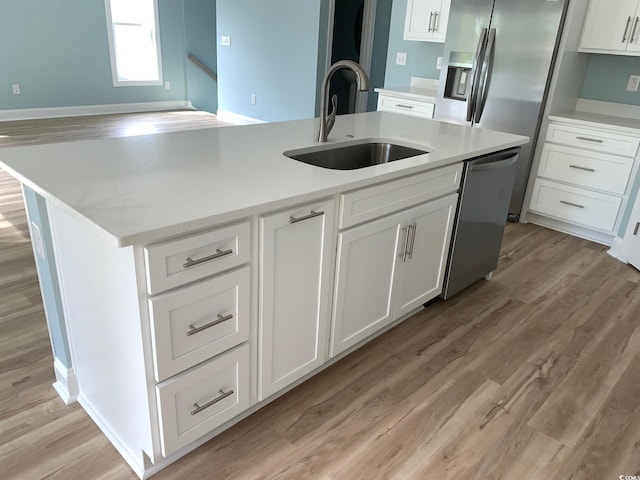 kitchen featuring appliances with stainless steel finishes, white cabinetry, an island with sink, sink, and light stone counters