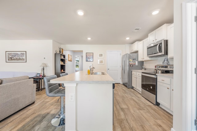 kitchen with a kitchen bar, an island with sink, white cabinets, and appliances with stainless steel finishes