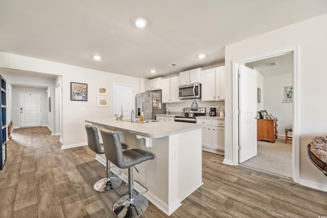 kitchen featuring white cabinetry, wood-type flooring, a kitchen breakfast bar, a kitchen island with sink, and stainless steel appliances