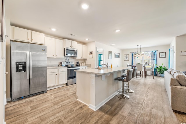 kitchen with a breakfast bar, white cabinetry, a kitchen island with sink, stainless steel appliances, and decorative light fixtures