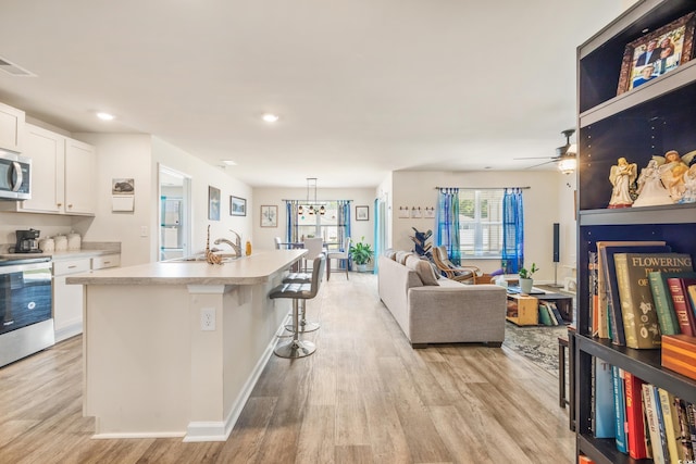 kitchen featuring pendant lighting, white cabinetry, stainless steel appliances, a center island with sink, and light wood-type flooring