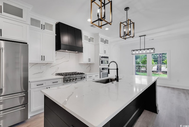 kitchen with premium range hood, white cabinetry, hanging light fixtures, an island with sink, and stainless steel appliances