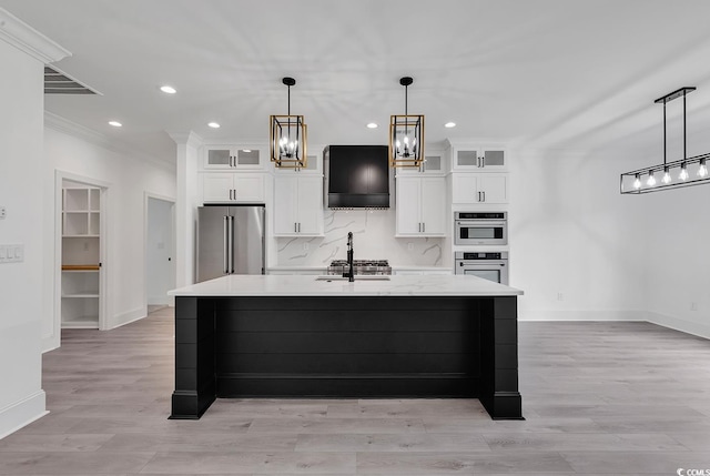 kitchen featuring appliances with stainless steel finishes, decorative light fixtures, decorative backsplash, sink, and a kitchen island with sink