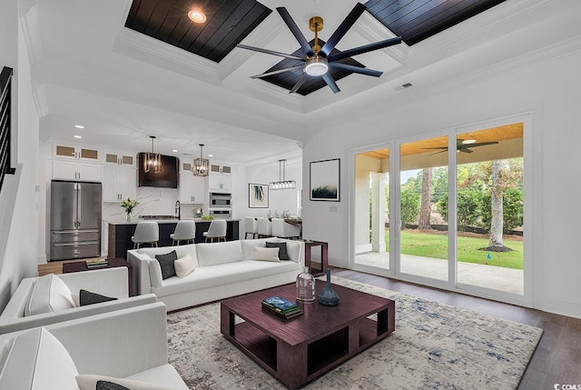 living room featuring an inviting chandelier, dark wood-type flooring, coffered ceiling, and ornamental molding