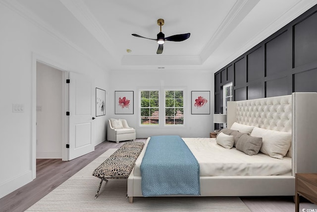 bedroom with ceiling fan, wood-type flooring, a tray ceiling, and ornamental molding