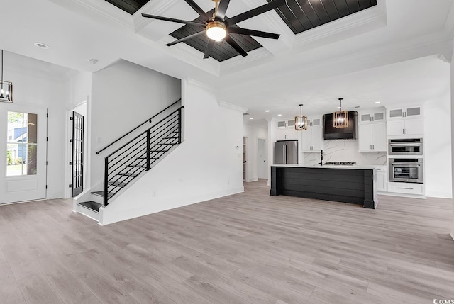 unfurnished living room featuring beamed ceiling, coffered ceiling, light hardwood / wood-style flooring, ornamental molding, and ceiling fan with notable chandelier