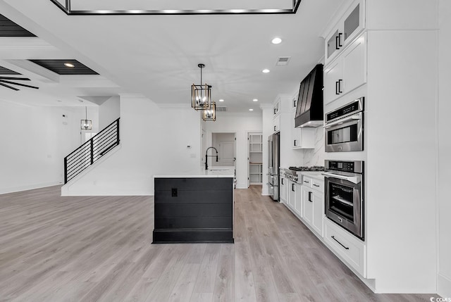 kitchen with decorative light fixtures, white cabinetry, a center island with sink, and stainless steel appliances