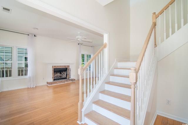 staircase with a brick fireplace, wood-type flooring, and ceiling fan