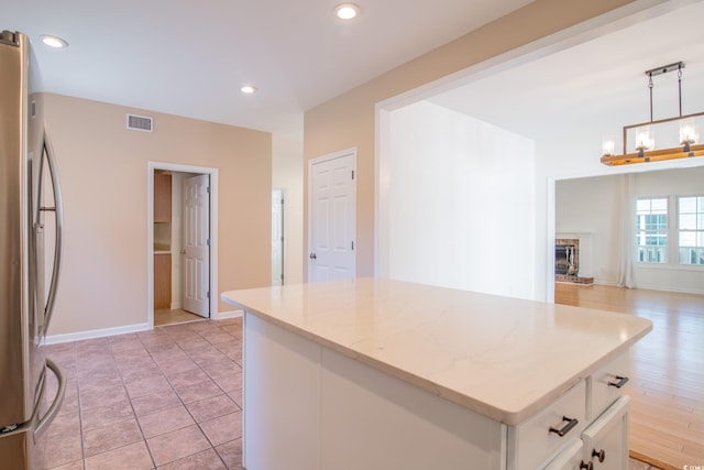 kitchen featuring a kitchen island, pendant lighting, white cabinets, light stone counters, and stainless steel refrigerator