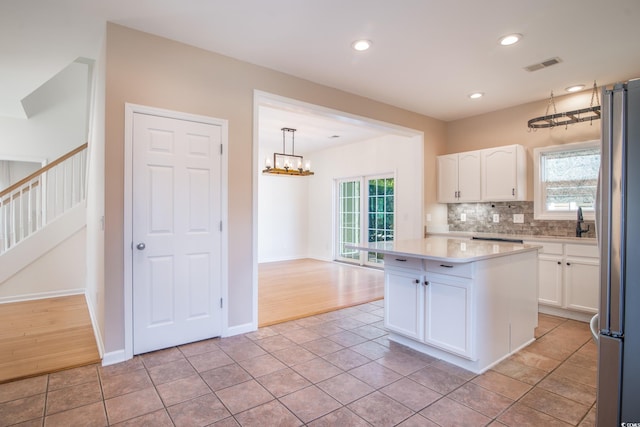 kitchen with stainless steel fridge, a center island, pendant lighting, light tile patterned floors, and white cabinets