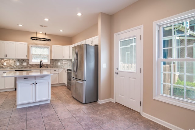 kitchen featuring white cabinets, a kitchen island, appliances with stainless steel finishes, light tile patterned floors, and backsplash