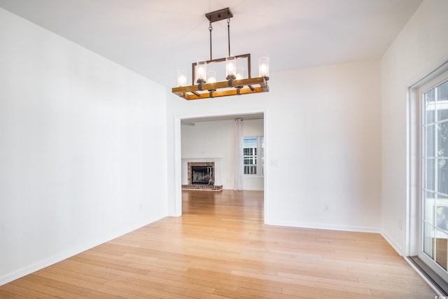 interior space with a notable chandelier, a brick fireplace, and light wood-type flooring