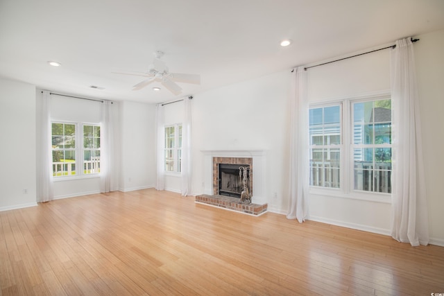 unfurnished living room featuring ceiling fan, a brick fireplace, and light wood-type flooring