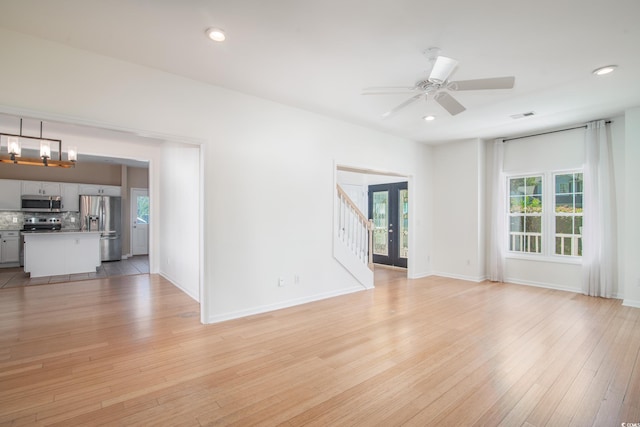 spare room with ceiling fan with notable chandelier and light hardwood / wood-style floors