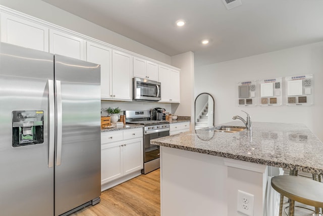 kitchen featuring sink, stainless steel appliances, light stone counters, light hardwood / wood-style floors, and white cabinets