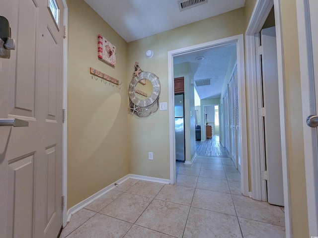 corridor with a textured ceiling and light tile patterned floors