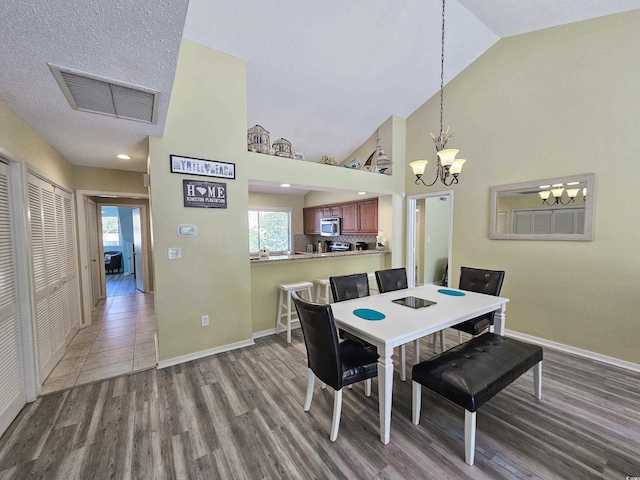 dining room featuring a textured ceiling, light hardwood / wood-style floors, a chandelier, and high vaulted ceiling