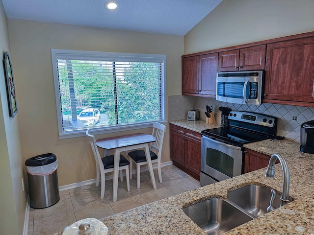 kitchen featuring vaulted ceiling, appliances with stainless steel finishes, light stone counters, and sink