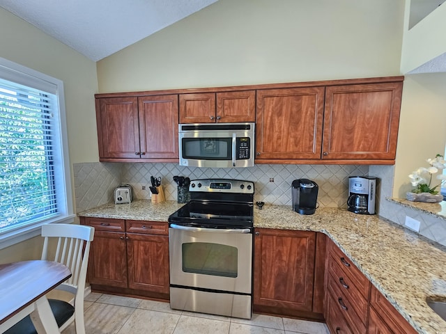 kitchen featuring lofted ceiling, light stone countertops, stainless steel appliances, and tasteful backsplash