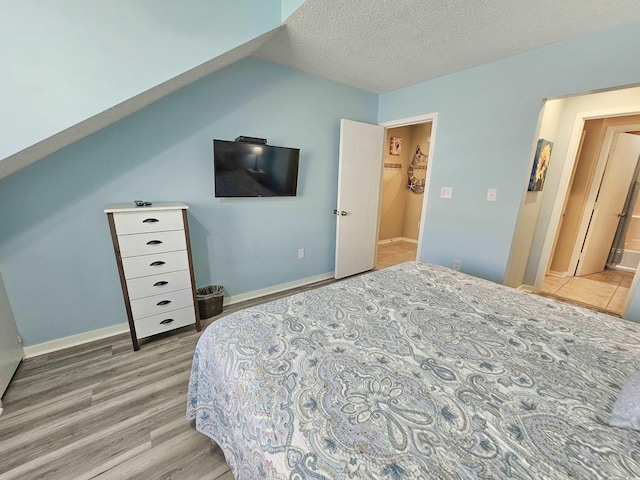 bedroom with a textured ceiling, light hardwood / wood-style flooring, and lofted ceiling