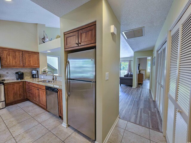 kitchen with a textured ceiling, sink, lofted ceiling, appliances with stainless steel finishes, and light tile patterned floors