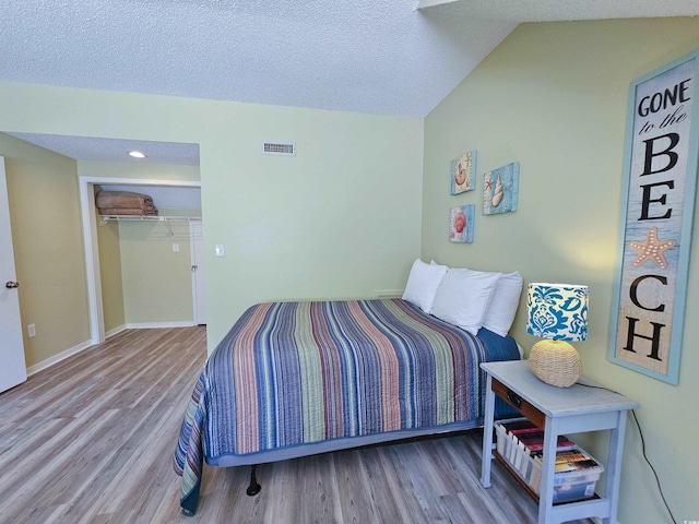 bedroom featuring vaulted ceiling, a textured ceiling, light hardwood / wood-style flooring, and a closet