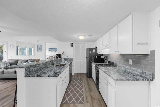 kitchen featuring a sink, white cabinets, open floor plan, a kitchen breakfast bar, and appliances with stainless steel finishes