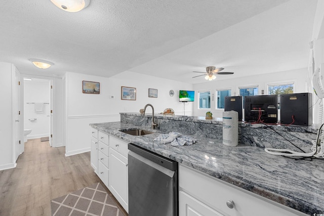 kitchen featuring stainless steel dishwasher, a textured ceiling, light wood-style floors, white cabinetry, and a sink