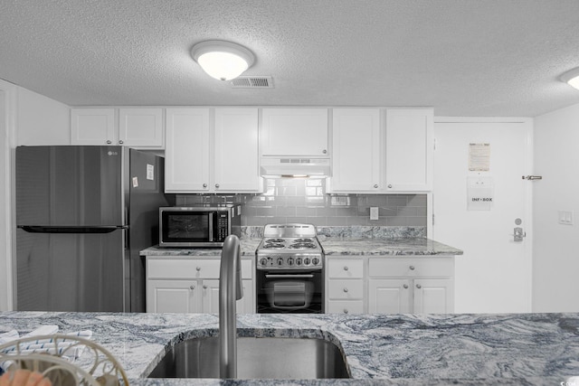 kitchen with light stone counters, under cabinet range hood, stainless steel appliances, a sink, and backsplash