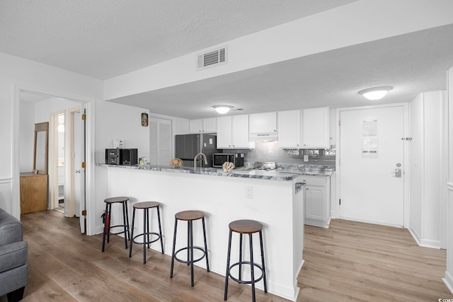 kitchen featuring white cabinets, appliances with stainless steel finishes, visible vents, and a kitchen breakfast bar