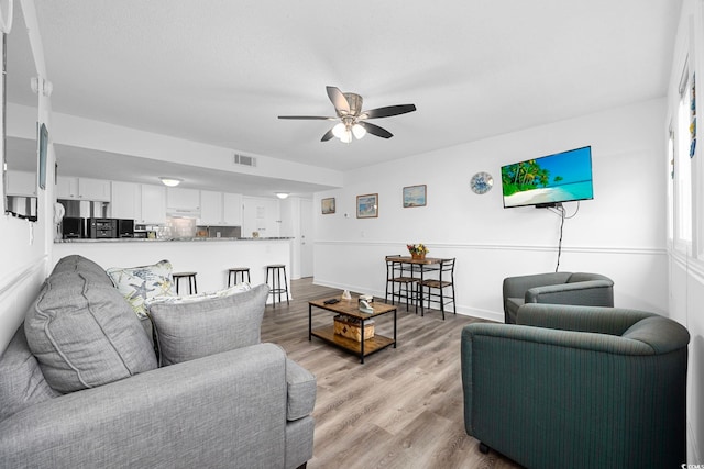 living room featuring baseboards, a ceiling fan, visible vents, and light wood-style floors