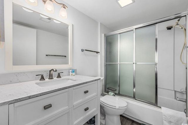 bathroom featuring toilet, combined bath / shower with glass door, visible vents, and vanity