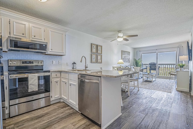 kitchen with white cabinets, sink, decorative backsplash, appliances with stainless steel finishes, and kitchen peninsula