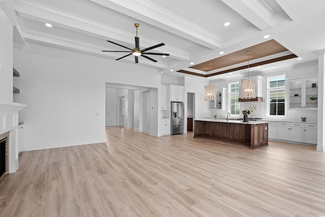 unfurnished living room with crown molding, sink, ceiling fan with notable chandelier, and light hardwood / wood-style flooring