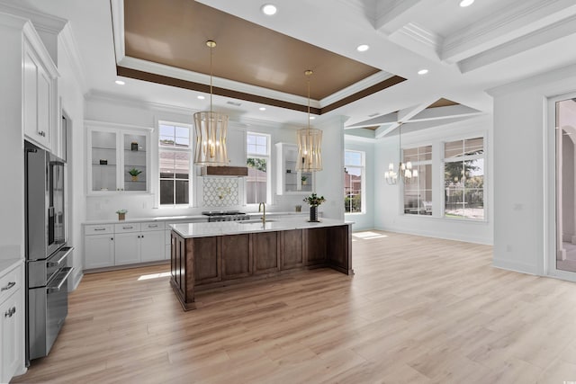 kitchen with white cabinetry, an island with sink, stainless steel fridge, a notable chandelier, and custom range hood