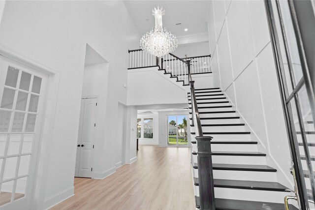 stairway with crown molding, wood-type flooring, a towering ceiling, and an inviting chandelier