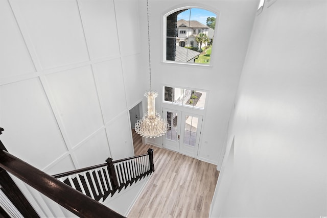 staircase featuring a high ceiling, an inviting chandelier, hardwood / wood-style floors, and french doors