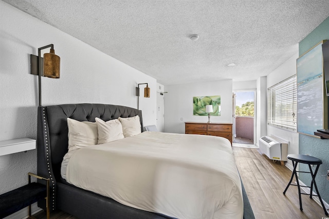 bedroom featuring hardwood / wood-style floors, a textured ceiling, and a wall mounted AC